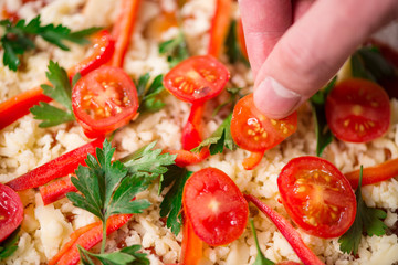 Bakers hands putting vegetables on the pizza. The concept of Italian cuisine.