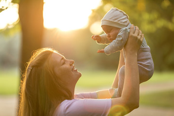 Young mother holds up two-month-old newborn baby in the summer green park. Moments of happy...