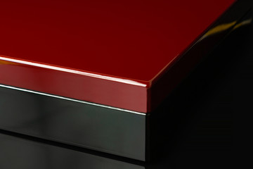 A lacquered gift box stands on a black glossy glass in which its reflection is visible