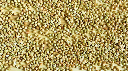 Background from raw organic green buckwheat porridge, vegan food. Texture of scattered buckwheat groats. Seeds are triangular in shape. Organic food. The concept of diet, weight loss, healthy eating.