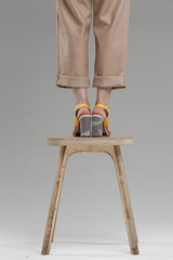 Legs in shoes of beautiful young woman standing on chair against plain wall, no brand, copy space