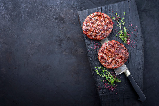 Gegrillte Wagyu Hamburger mit Rotwein Salz und Kr&auml;uter als Draufsicht auf einem verkohlten Holz Board mit Textfreiraum links