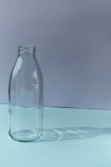 Glass bottle stands on a blue table against the background of a white wall shadow from the bottle sunny