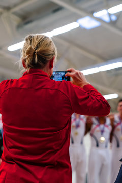 The coach of a winning team taking their picture with a phone the podium after winning the competition. You can see the team wearing gold medals.