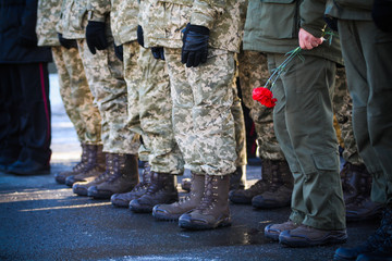 The military stand in a row and one of them holds flowers in his hands
