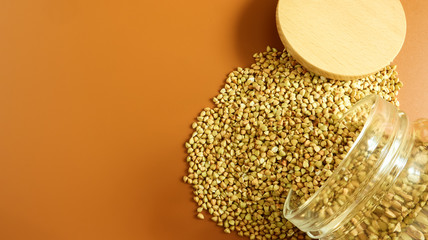 Scattered raw green buckwheat with a glass jar for cereals. Vegan organic food concept. The concept...