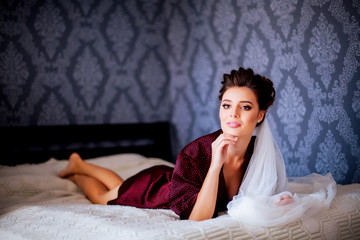 Gorgeous bride in dress lying on bed in luxurious room while preparing for wedding ceremony