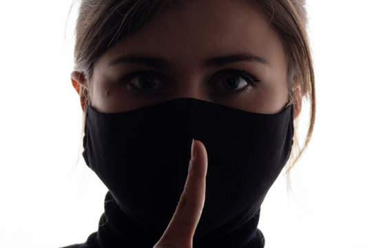 silhouette profile of young woman in protective mask showing gesture silence on dirty green background, girl with finger near mouth shh, concept silence of truth, information secrecy