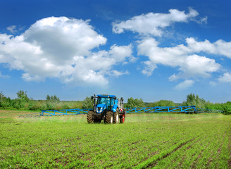 Obraz premium new blue tractor in field work with trailed sprayer, winter crop fertilizers, spring crop fertilizers