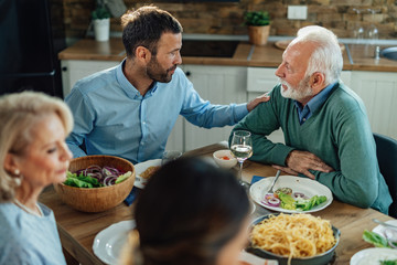 Senior man and his adult son communicating at dining table.