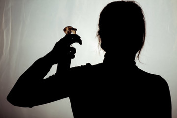woman in protective mask holding up bottle of disinfectant spray near the head on dirty green...