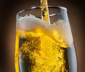 Jet of beer is poured into a beer glass, causing a lot of bubbles and foam.