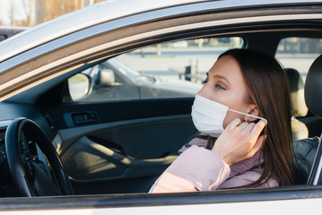 A young girl sits behind the wheel in the car in the mask during the global pandemic and coronavirus. Quarantine