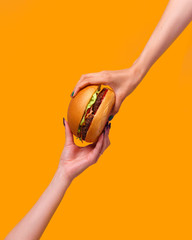 cropped image of female hands holding burger against yellow background