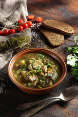 Rustic soup with vegetables, meat and fresh herbs in a clay bowl on an old wooden background. Bread, cumin, coriander, tomatoes, spoons and a bunch of dill. Background image, copy space