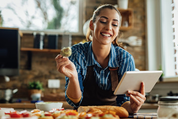 Happy woman preparing food while using touchpad in the kitchen.