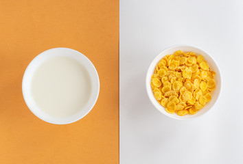 Flat lay with cornflakes and milk in white bowls on double beige background, top view. Concept of healthy breakfast