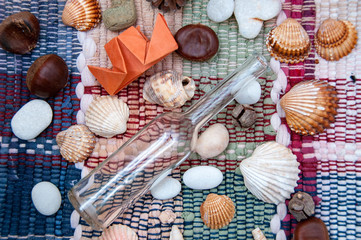 Paper ship, wine bottle, seashells and pebbles on colorful tissue patchwork carpet. Traveling concept. Vacation concept. Colorful flat lay design. Origami ship