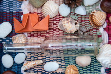 Paper ship, wine bottle, seashells and pebbles on colorful background. Traveling concept. Vacation concept. Colorful flat lay design. Origami ship