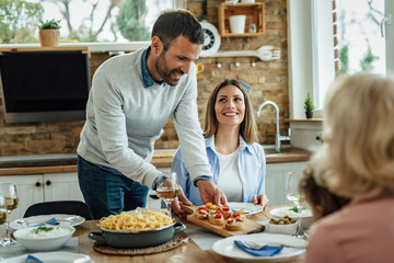 Happy man serving appetizer while having lunch with his family.