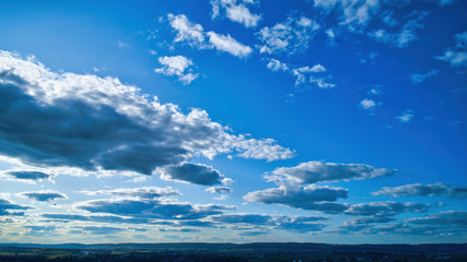 Naklejka na ściany i meble Blue sky and multiple clouds background showing a horizon and a hidden sun
