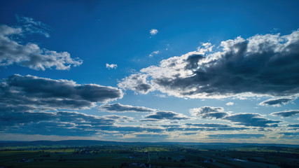 Blue sky and multiple clouds background showing a horizon and a hidden sun