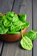 Spinach leaves in wooden bowl on dark rustic background. Healthy vegan food concept. Eco-conscious vegan lifstyle.