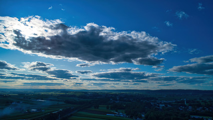 Blue sky and multiple clouds background showing a horizon and a hidden sun