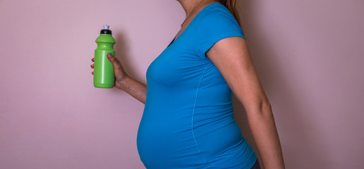 Beautiful pregnant brunette woman drinking water from the bottle on isolated pink background