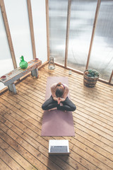Young woman in seated position. Yoga practice at home studio due to COVID-19.  Care about our mental and physical  health in quarantine. Cosy, bright and wooden interior. 
