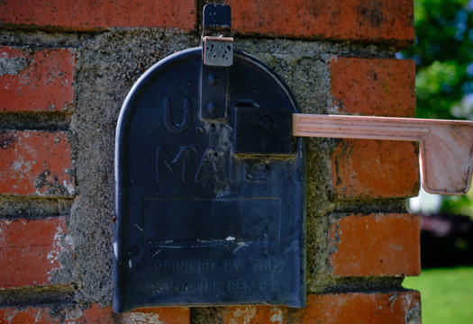 Black mailbox set into red brick with green background - Powered by Adobe