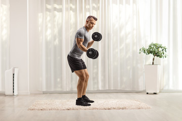 Naklejka premium Young fit man lifting dumbbells at home