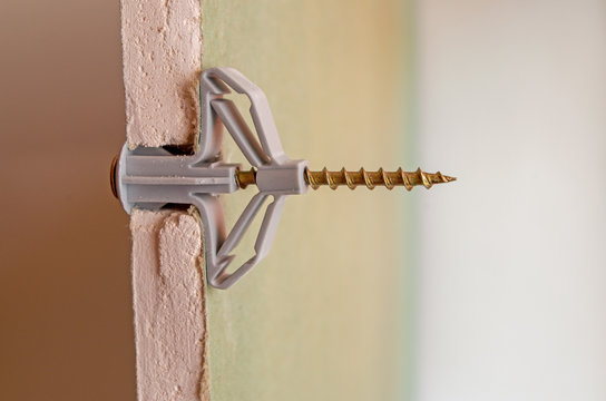 Grey plastic butterfly-type dowel fixed in a pre-drilled hole in a sheet of moisture-resistant drywall, split view. Sheet is cut at installation site, showing the gypsum fiber and connection details.
