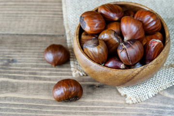 Heap of chestnuts in the bowl on the wooden kitchen background. Healthy fruit chestnuts, vitamins.