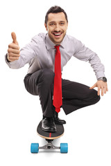 Young businessman kneeling and riding a skateboard and showing thumbs up © Ljupco Smokovski