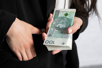 The woman holds her right hand in her pocket and squeezes a thick bundle of banknotes in her left.