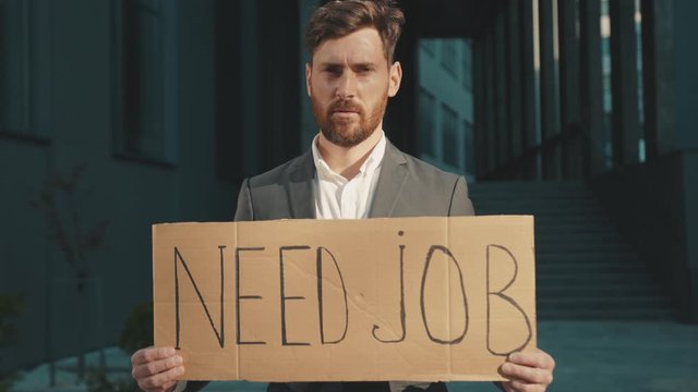 Portrait young businessman holding poster cardboard with Need Job jobless message sign coronavirus crisis text job showing professional finance economy slow motion