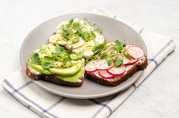 Variety of mini sandwiches with cream cheese and vegetables on a gray plate, light background.