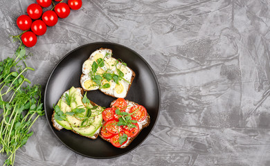 Variety of mini sandwiches with cream cheese and vegetables on a black plate, dark background.