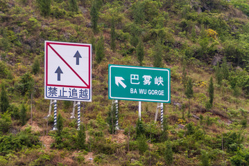 Wuchan, China - May 7, 2010: Dawu or Misty Gorge on Daning River. Boat traffic signs on steep green foliage hill. Ba Wu or Dawu white on green. Blue and red directional arrows on white.