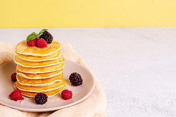 Homemade classic American pancakes with fresh raspberries, blackberries, honey and mint leaves, on a light background.