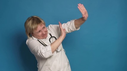 Eldery caucasian doctor lady in white coat on blue background. She wear stethoscope and scares of something