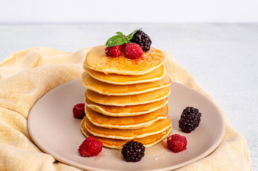 Homemade classic American pancakes with fresh raspberries, blackberries, honey and mint leaves, on a light background.
