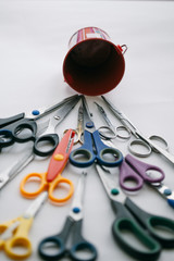 Many multi-colored stationery scissors heading towards the red bucket