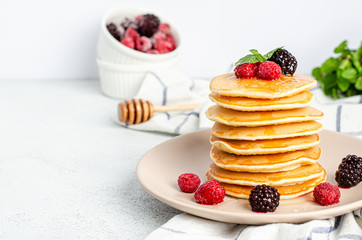 Homemade classic American pancakes with fresh raspberries, blackberries, honey and mint leaves on a grater, light background.