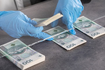 Hands of young cashier in protective gloves hand over bundles of banknotes.