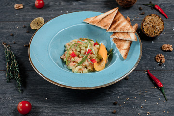 sresh salmon salad and toasted bread in blue plate on grey served table. traditional dish menu served in a restaurant