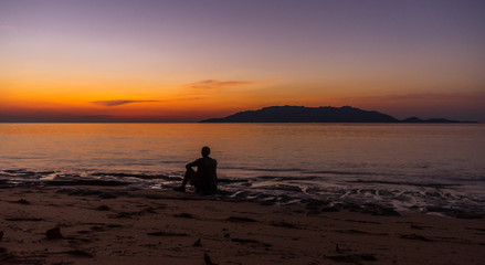 Fototapeta premium Person sitting and enjoying evening sunset scene with Banda Besar island in distance very bright vibrant sky in Hatta