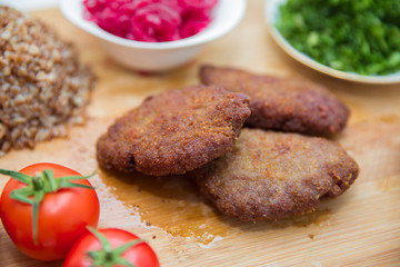 Meat cutlets, baked buckwheat on a board . Red cabbage sauerkraut . Garlic, Onion, Tomatoes. Chopped coriander. Homemade cutlets with oatmeal on a table . Meat cutlets on a wooden skewer .