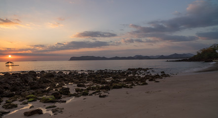 Nice sunset or sunrise moment sunbeam goes through rocky beach scene with hills in distance in Sumbawa, Indonesia